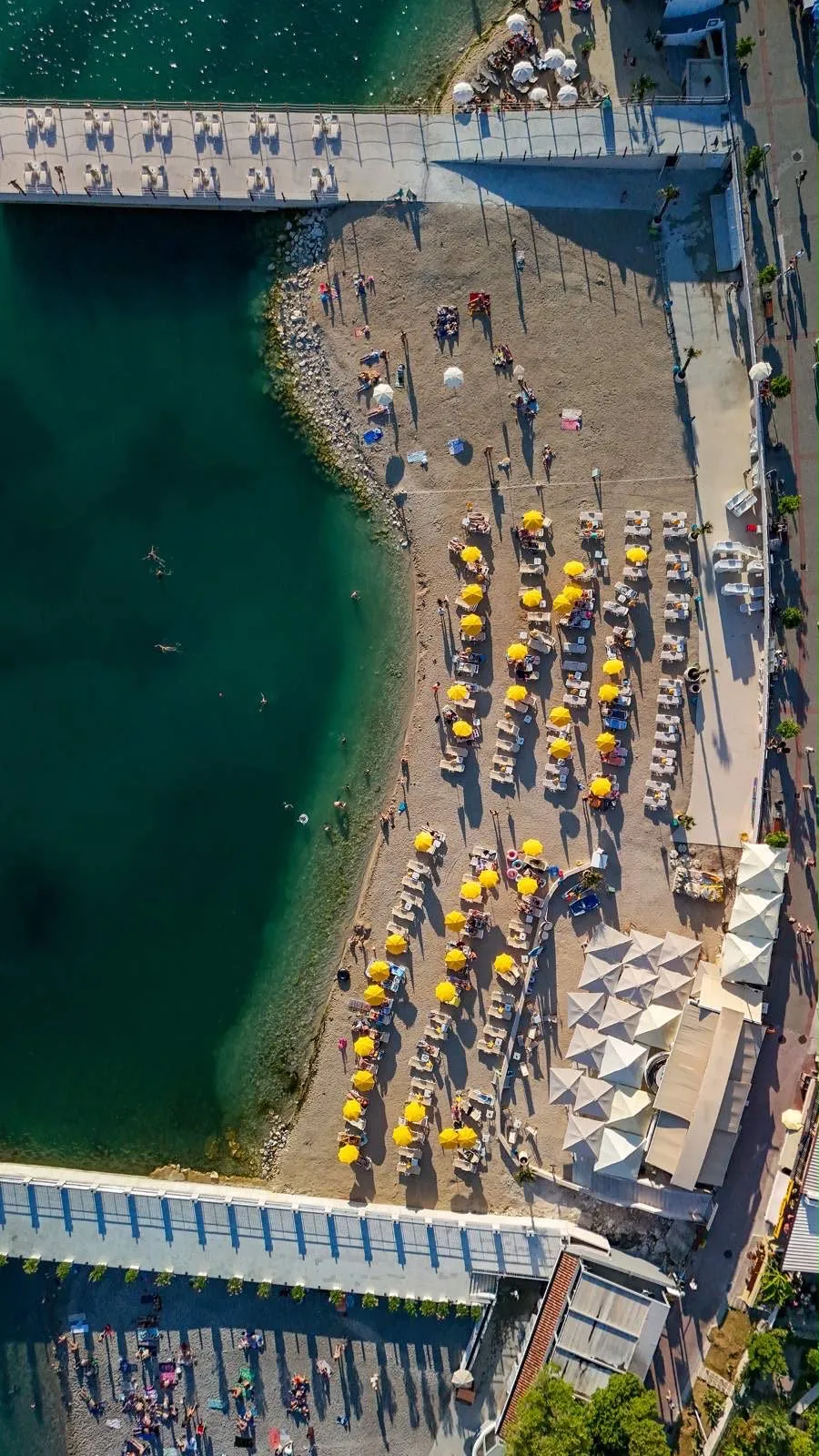 Redovi ležaljki i suncobrana iz vazduha, iznad tirkizne plićine