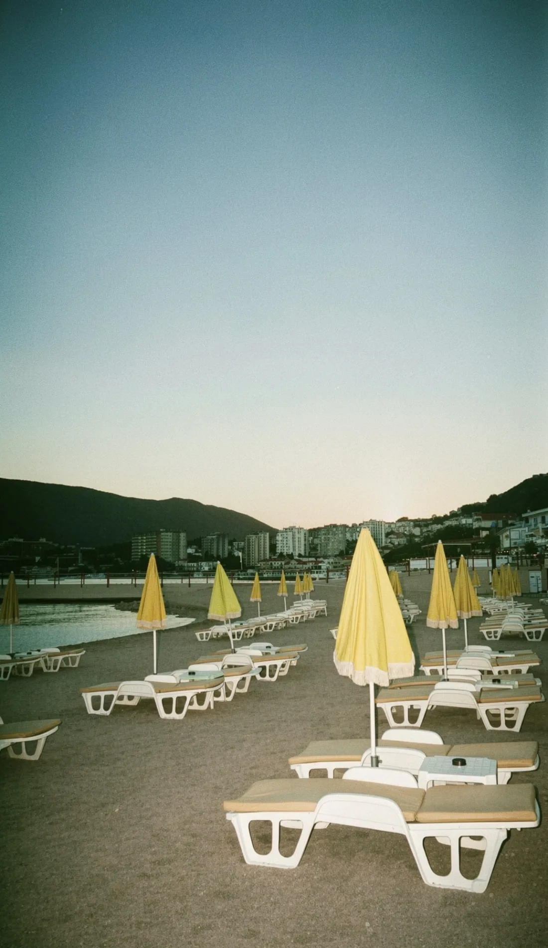 Ležaljke i sklopljeni žuti suncobrani na praznoj plaži u sumrak